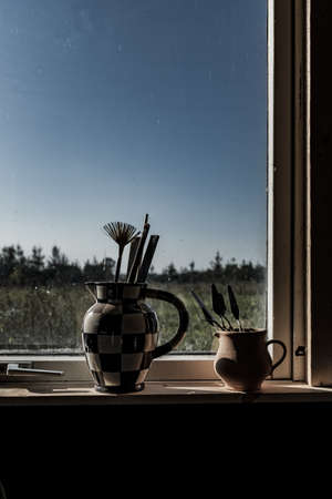 A vertical shot of two vases near the window filled with art supplies with the background of...