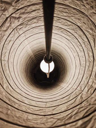 The inside of a lampshade with a white lightbulb turned on in a dark roomの写真素材