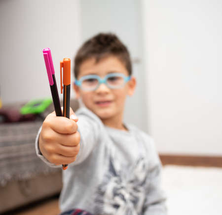 A selective focus shot of a little boy with glasses showing the colorful markersの写真素材