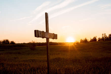 A closeup shot of a wooden cross in a grassy field with the sun shining in the backgroundの写真素材