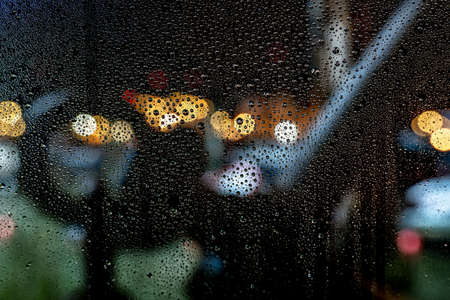 A beautiful shot of water drops on a window during a rainy night with a blurred backgroundの写真素材