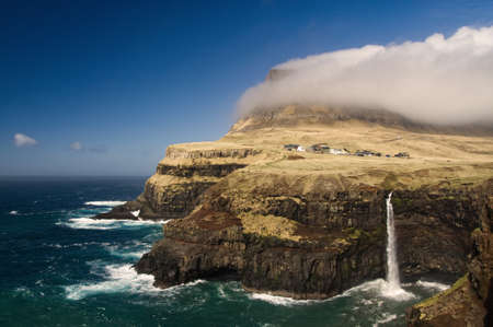 A beautiful shot of the Vagar cliff near the sea with a blue sky in the backgroundの写真素材