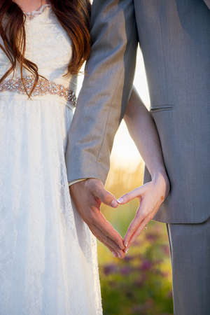 A vertical shot of the bride and the groom making a heart shape with their handsの写真素材