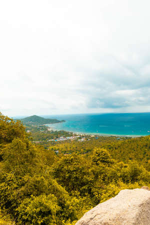 A vertical shot of hills covered in trees near the sea under a cloudy skyの写真素材