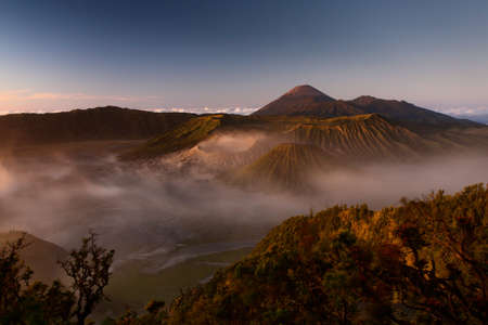 A horizontal shot of the beautiful Bromo volcano covered in fog under the clear sky