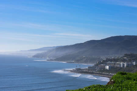 A high angle shot of an ocean shore with a beautiful green scenery next to a mountain