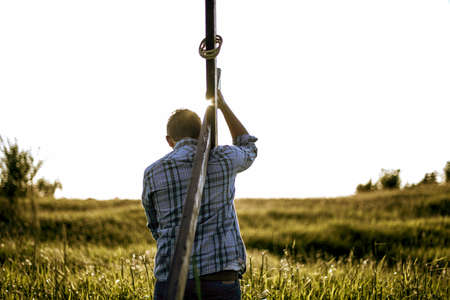 A male carrying a hand made wooden cross in a grassy field shot from behindの写真素材