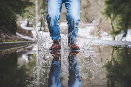 Male legs wearing blue jeans and brown boots walking on the wet streetの写真素材