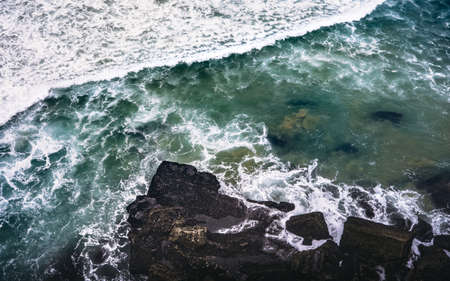 An overhead shot of a rocky shore near a body of water with rocks splashing on the rocks. Perfect for a wallpaper or a background.の写真素材