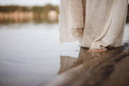 A closeup shot of a person wearing a biblical robe walking on the shorelineの写真素材