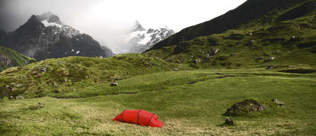 A contrasting scenery of a green view with a red tent in the middle  next to gloomy mountains