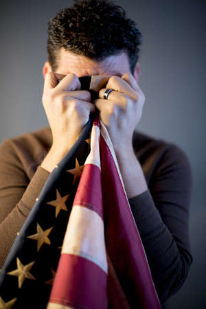 A vertical closeup shot of a retired soldier cleaning his tears with the unites states flagの写真素材