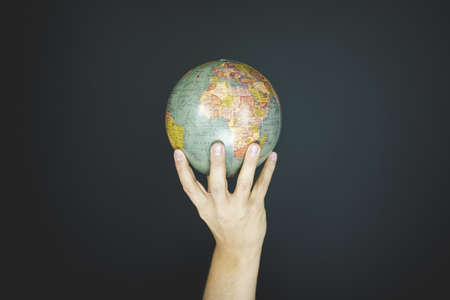 A closeup shot of a person holding a small globe with a black backgroundの写真素材