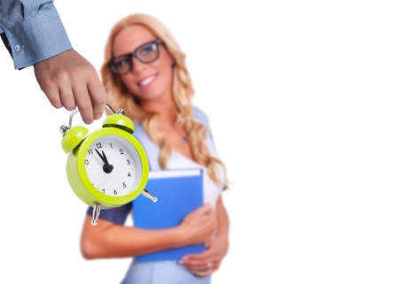 A child's hand holding a yellow alarm clock in front of a caucasian blonde woman wearing glasses and...