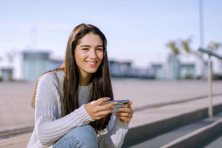 A closeup shot of a happy brunette with a wide smile using her cellphone isolated on a blurred...