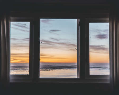 A horizontal shot of a body of water during sunset through a window. Perfect for a wallpaper or a background.の写真素材