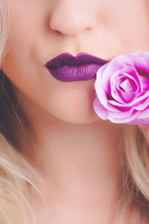 A closeup shot of a female wearing purple lipstick with pink rose close to her lips - great for a fashion articleの写真素材