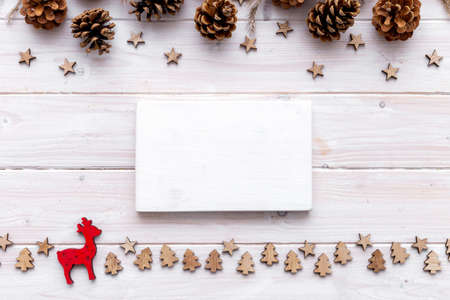 A blank white piece of wood surrounded by small Christmas decorations on a wooden table