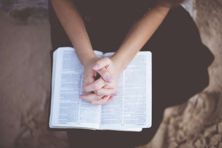 An overhead shot of a female praying with her hands on the bible