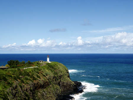 A beautiful view of a lighthouse on a grass covered cliff over the ocean under the cloudy skyの写真素材