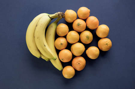 A closeup shot of oranges and banana making a heart shape on a dark blue surface