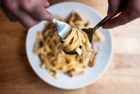A high angle closeup shot of a person reeling up the pasta with a spoon and a fork