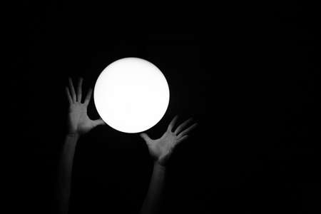 The human hands trying to catch an enlightened white circle on black backgroundの写真素材