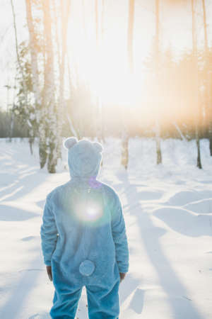A vertical shot of a person in a fluffy blue costume standing in the snowy forest and enjoying the sunlight - escape from the reality conceptの写真素材