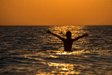 A beautiful scenery of female swimming in the ocean during a breathtaking sunsetの写真素材