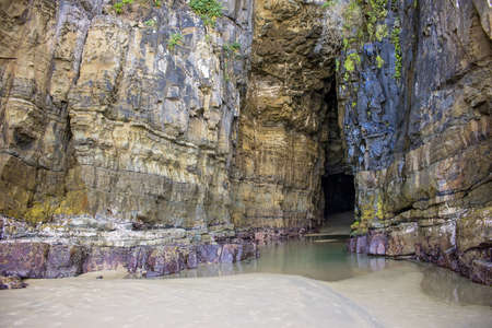 A landscape of a cave with high stone walls covered in greenery surrounded by water