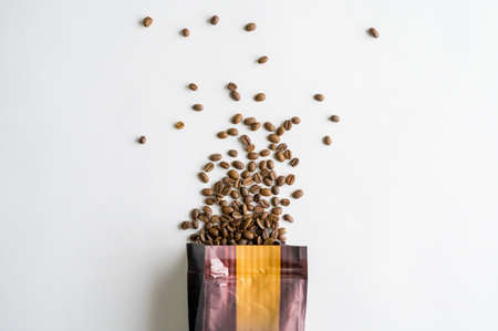 An overhead shot of coffee beans spilling out of the bag on a white surface