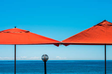 A beach resort with two red parasols with a reflective crystal ball in the middle - great for a backgroundの写真素材