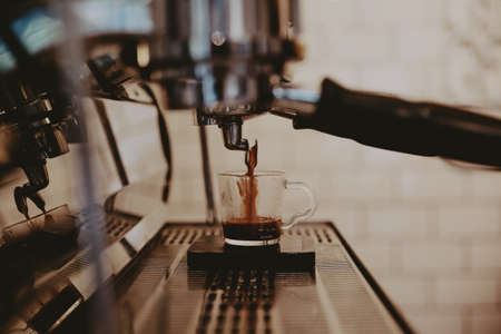 A closeup of a metal coffee machine pouring coffee into a glass cup