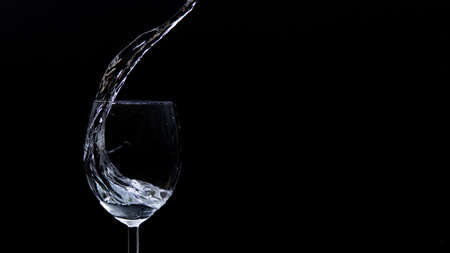 Wine glass on a pitch-black background with liquid pouring in it from aboveの写真素材