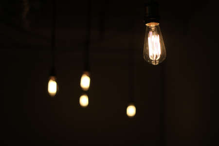 A closeup shot of a light bulb hanging in a dark room with a blurred backgroundの写真素材