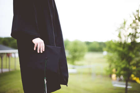 A shallow focus shot of a graduate holding its hat with a blurred backgroundの写真素材