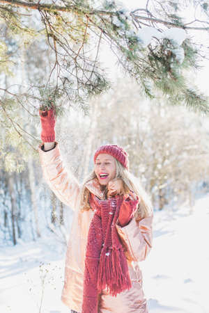 A vertical shot of a blonde female in enjoying the winter miracle during the snowflake in a forest