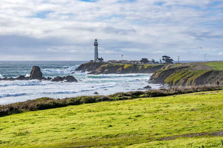 A beautiful shot of a lighthouse on a green rock formation at the ocean shoreの写真素材