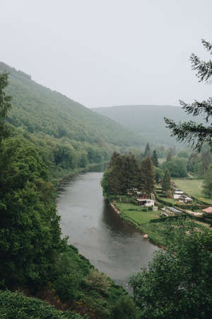 A vertical shot of a river surrounded by foggy mountains captured in Belgium