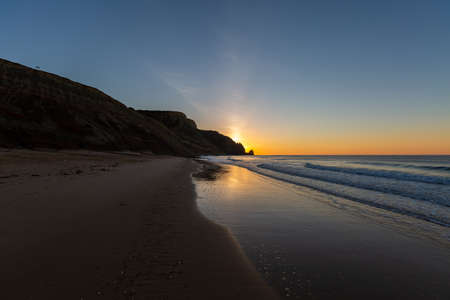 A landscape of the sea surrounded by rocks under a blue sky and sunset reflection in Portugalの写真素材
