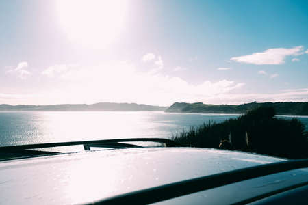 A landscape from a car roof of a lake surrounded by greenery and an island under a blue sky