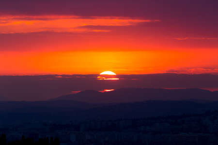 A beautiful scenery of cityscape surrounded by rocky mountains with the stunning view of sunset in the backgroundの写真素材