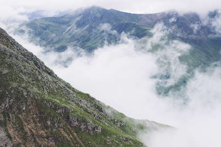 A scenery of smoke coming out of the mountains in the middle of a green view