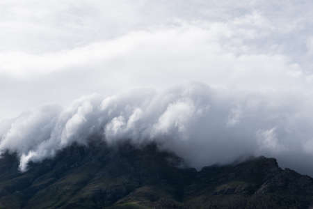 A breathtaking shot of the white clouds covering the dark hills