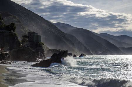 A beautiful shot of waves splashing to the shore surrounded by mountains at the Italian shore