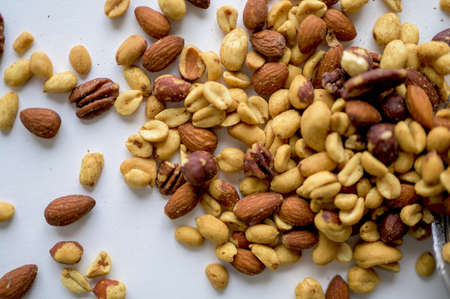 An overhead shot of different types of nuts on top of each other on a white surface