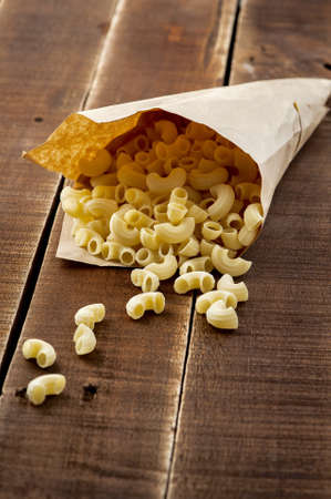 A closeup shot of paper bag full of raw macaronis laid on a wooden surface