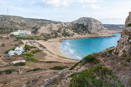 A landscape of a sea in Greece surrounded by mountains greenery and buildings under a cloudy sky