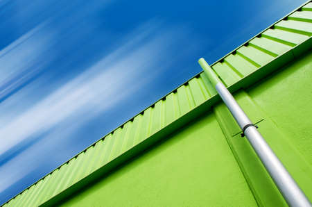 A low angle shot of a green building with a gray pipe under the cloudy skyの写真素材