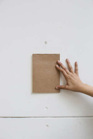 A vertical shot of a person holding a brown notepad on a white wallの写真素材
